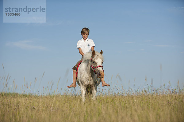 Mädchen reitet auf einem Pony über eine Wiese