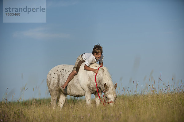 Mädchen reitet auf einem Pony über eine Wiese