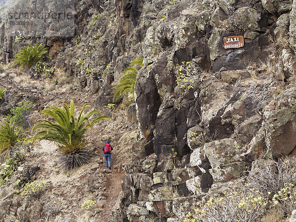 Frau mit Rucksack auf Wanderweg  Taxi-Schild mit Telefonnummer an Felswand  Barranco de Argaga  La Gomera  Kanarische Inseln  Kanaren  Spanien  Europa