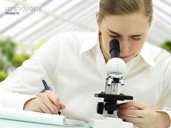 Wissenschaftlerin schaut durch Mikroskop im Treibhaus