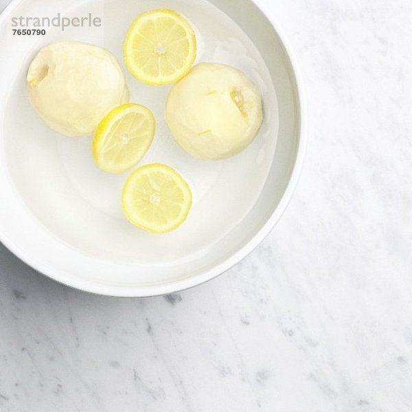 Zwei geschälte Quitten mit Zitronenscheiben in einer Schüssel mit Wasser