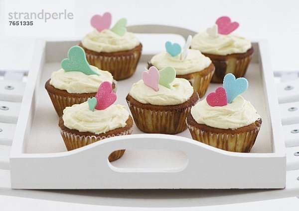 Vanille-Cupcakes mit Zuckerguss und Zuckerherzen auf Tablett