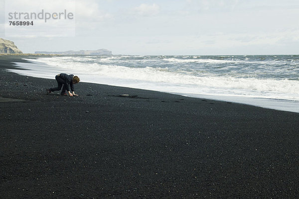 Junge  der den schwarzen Sandstrand aufliest  Island