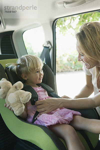 Frau befestigt kleines Mädchen im Autositz