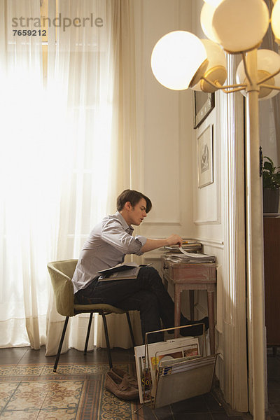Mann liest zu Hause am Schreibtisch