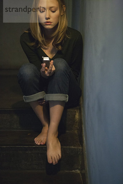 Junge Frau sitzt auf der Treppe und schaut auf das Handy.