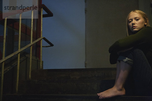 Junge Frau auf der Treppe sitzend  Knie umarmend