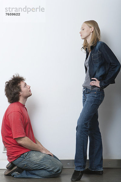 Junger Mann kniend vor wütender Freundin