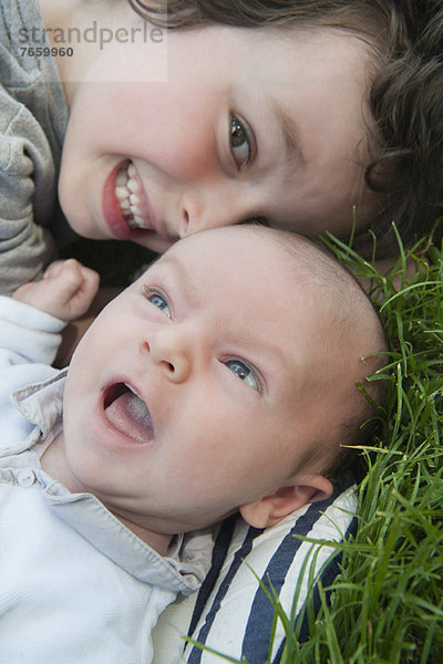 Junge auf Gras liegend mit kleinem Bruder  Portrait