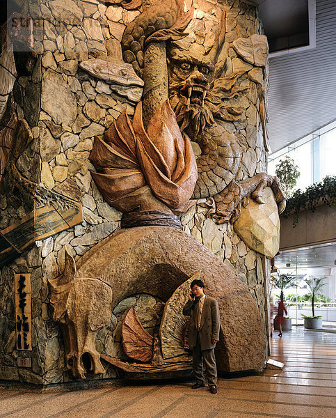 Lobby des Lippo Centre  Kunstwerk aus Stein  davor ein Mann mit Handy  Detail  Glasfassade  Central District  Victoria Island