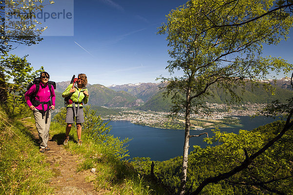 Zwei Frauen wandern am Höhenweg von den Monti di Vairano zu den Monti Caviano am Monte Gambarogno  Blick auf das Maggia-Delta  Ascona und Locarno  Tessin  Schweiz  Europa