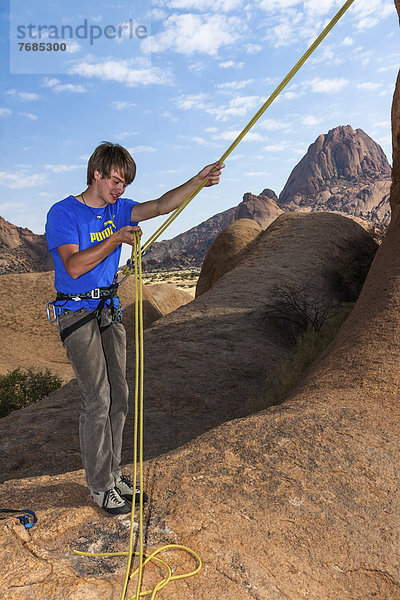 Junger Mann hängt im Kletterseil  Bogenfels  Spitzkoppe-Gebiet  Namibia  Afrika