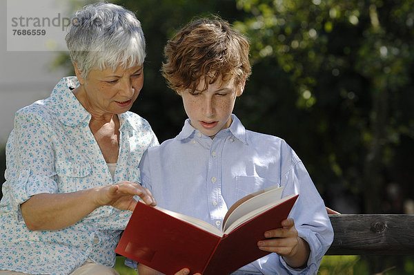 Oma und Enkel auf Parkbank schauen zusammen in ein rotes Buch