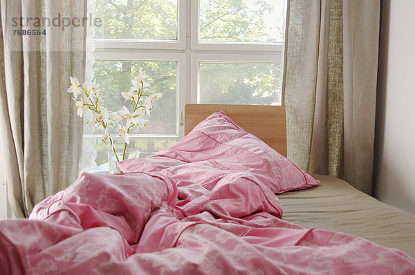 Bett am Fenster mit zerwühlter pinker Bettdecke