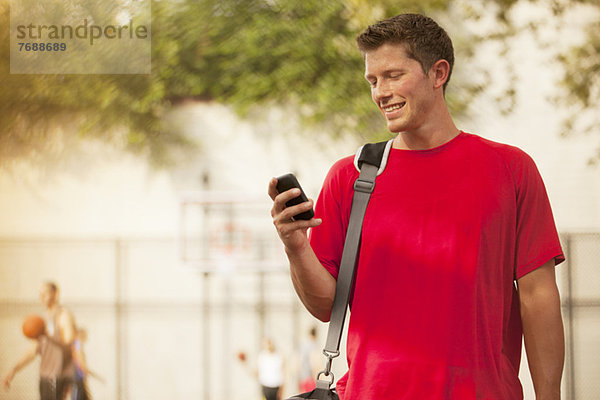 Mann mit Handy auf dem Basketballplatz