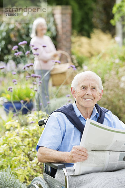 Älterer Mann im Rollstuhl beim Zeitungslesen im Freien