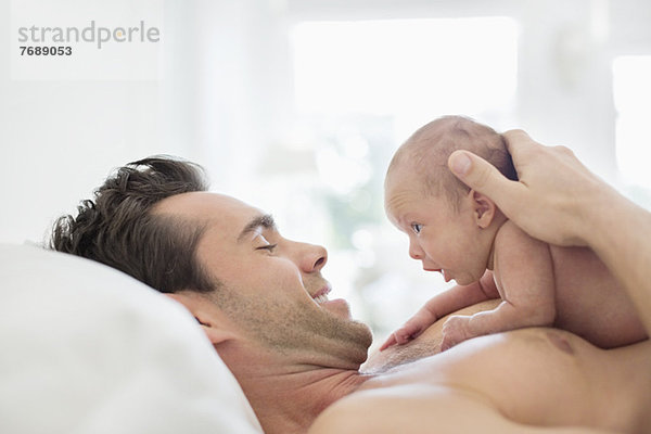 Vater wiegt Neugeborenes im Bett