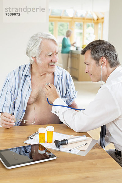 Der Arzt hört den Herzschlag des älteren Patienten beim Hausbesuch.