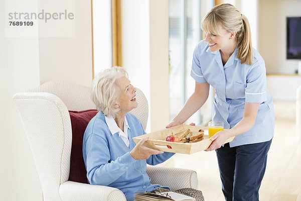Betreuerin gibt älteren Frauen Tablett mit Lebensmitteln