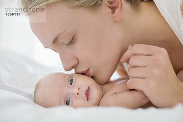 Mutter küsst Neugeborenes auf dem Bett