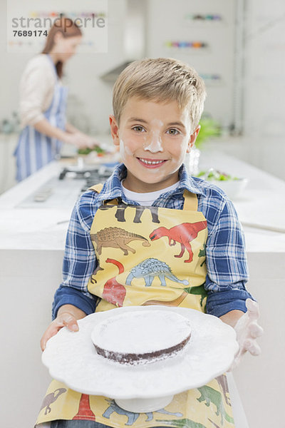 Junge mit Mehl bedeckt  der Kuchen in der Küche hält