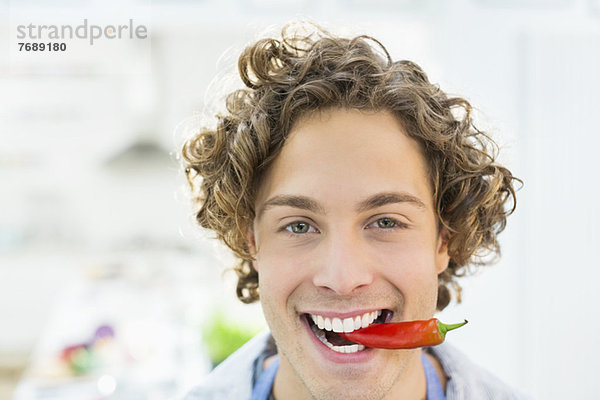 Lächelnder Mann mit Chilipfeffer im Mund