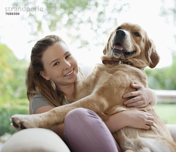 Lächelndes Mädchen umarmt Hund auf Sofa