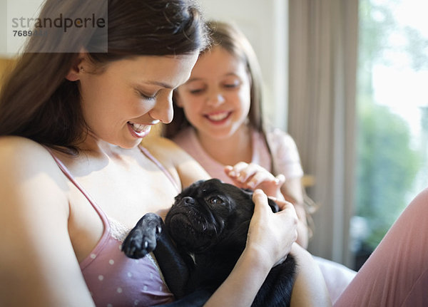 Mutter und Tochter streicheln Hund im Bett