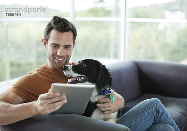 Mann streichelt Hund und benutzt Tablet-Computer