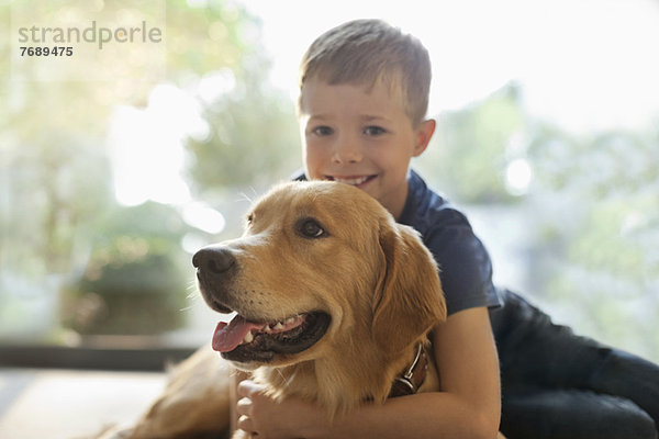 Lächelnder Junge umarmt Hund im Haus