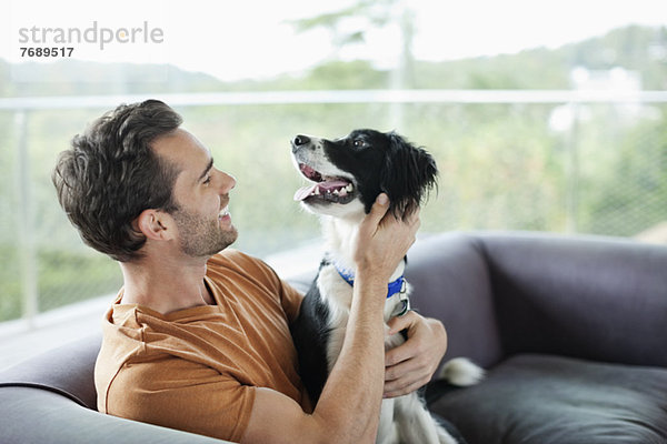 Lächelnder Mann streichelt Hund auf Sofa