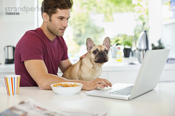 Mann am Laptop Streichelhund in der Küche