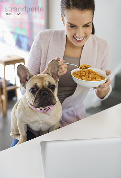 Frau isst Müsli mit Hund auf dem Schoß