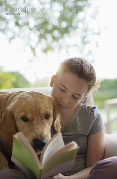 Mädchen lesen mit Hund im Sessel