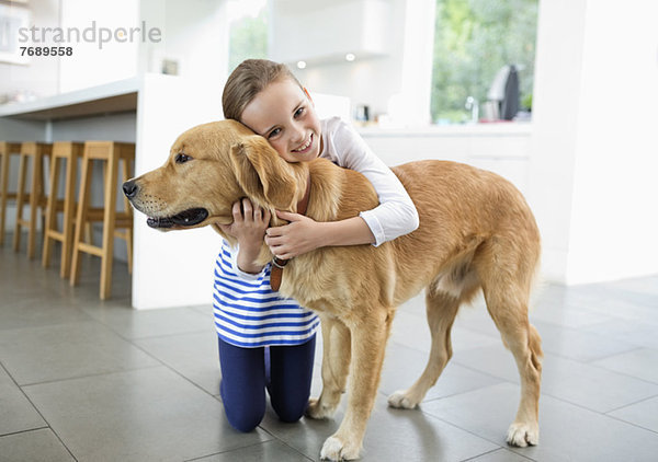 Lächelndes Mädchen umarmt Hund in der Küche