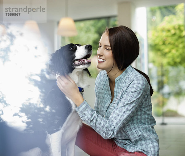 Lächelnde Frau streichelt Hund im Haus