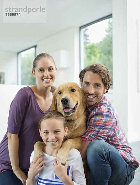 Familie lächelt mit Hund im Haus