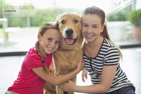 Lächelnde Mädchen umarmen Hund im Haus