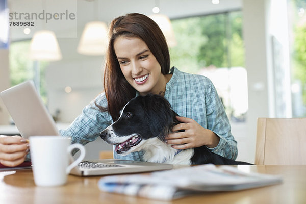 Frau mit Hund auf Schoß mit Laptop