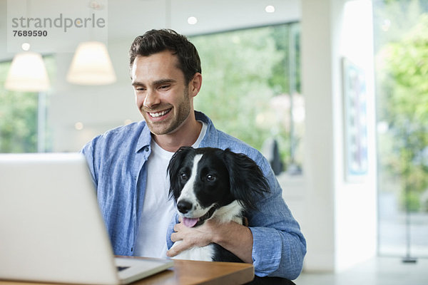 Mann mit Hund auf Schoß mit Laptop