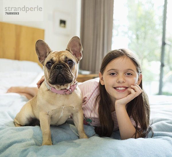 Lächelndes Mädchen entspannt mit Hund im Bett