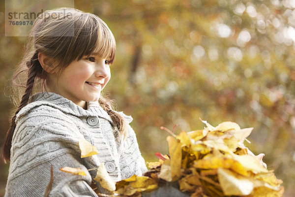 Lächelndes Mädchen spielt im Herbstlaub