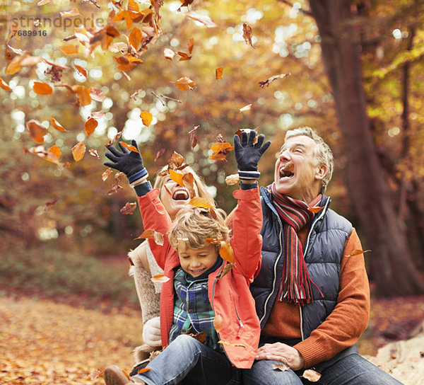 Älteres Paar spielt mit Enkel im Herbstlaub