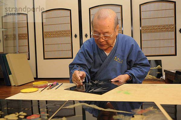 Japanischer Kunsthandwerker in seiner Werkstatt kratzt bis auf die Blattgoldschicht in die oberste Lackschicht ein Bambusmotiv hinein  Sabae  Fukui  Japan  Ostasien  Asien