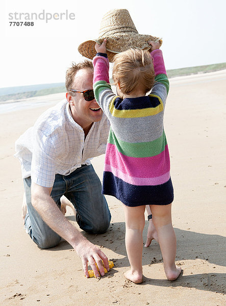 Mädchen mit Hut auf Vater am Strand