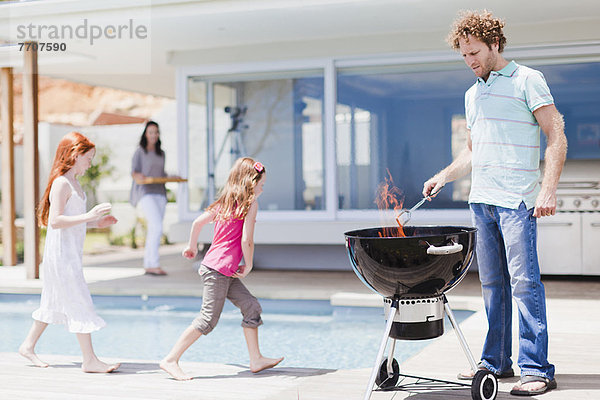 Mädchen am Pool als Vater grillt