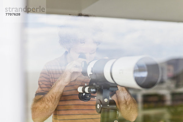 Mann mit Teleskop am Fenster