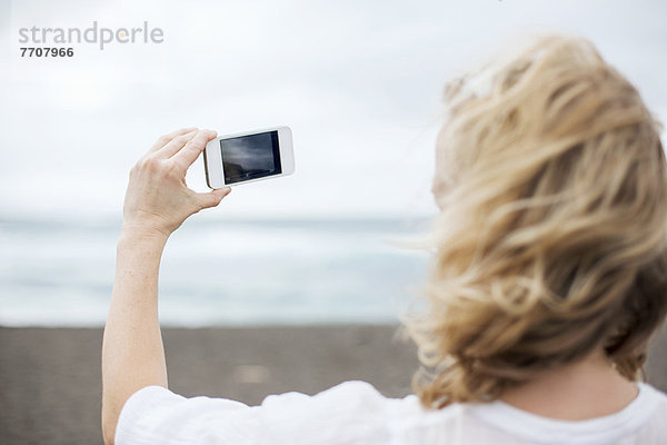 Frau macht Handyfoto am Strand
