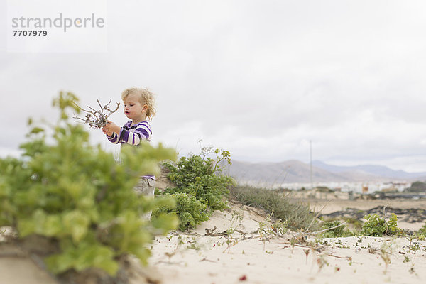 Mädchen spielt mit Zweigen am Strand