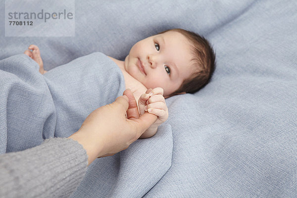 Baby Junge hält Mütter Finger im Bett